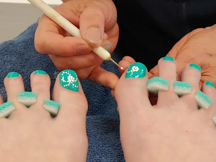 Hand painted flowers being dotted onto a teal nail